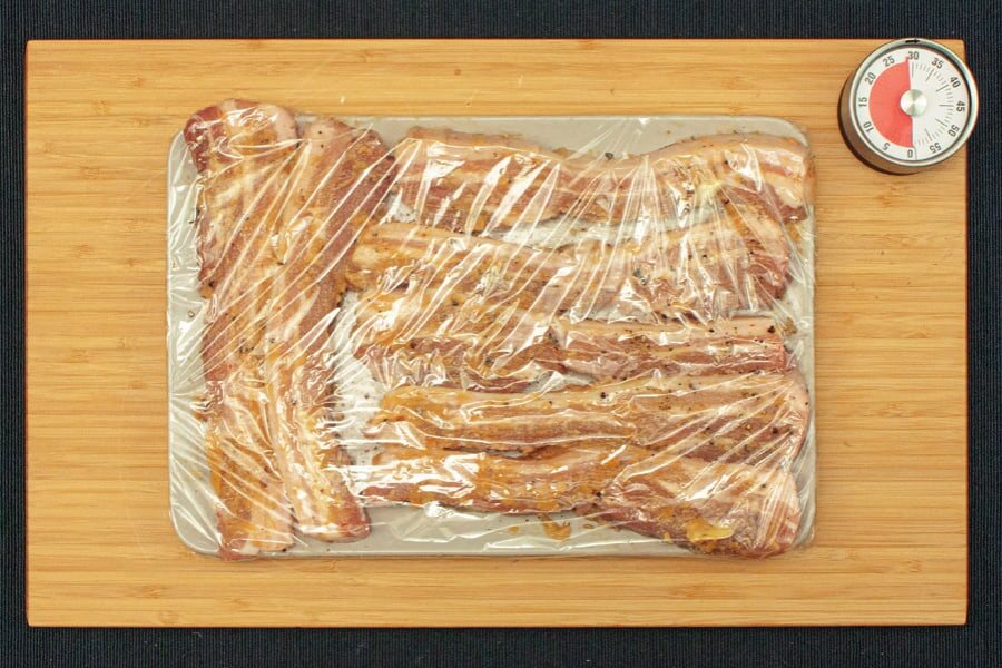 Mariniertes Fleisch unter Frischhaltefolie, daneben ein Küchenwecker