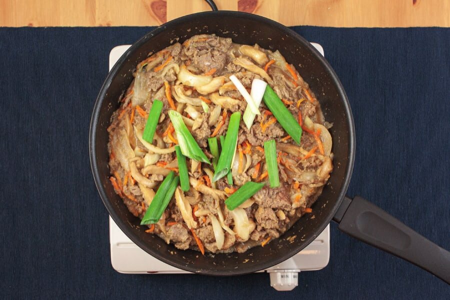 Pfanne mit fast garem Bulgogi, obenauf schräg geschnittene Frühlingszwiebeln