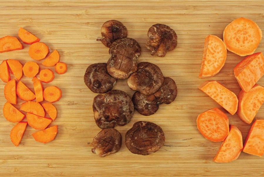 Karottenstücke, Shiitake-Pilze und Süßkartoffelstücke auf einem Holzbrett