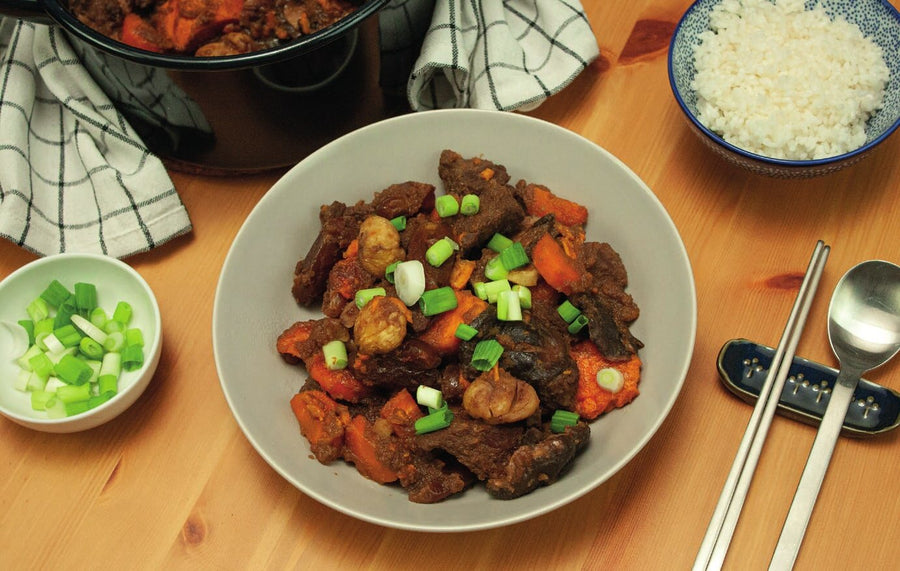 Angerichtetes Galbi-Jjim mit Frühlingszwiebeln, daneben Reis, Stäbchen und Löffel