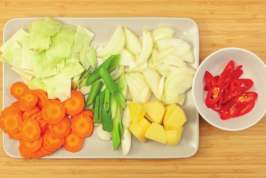 Geschnittener Weißkohl, Karottenscheiben, Frühlingszwiebel, Zwiebel und Kartoffelstücke auf einer Platte, daneben Chiliringe