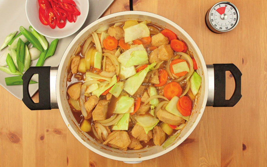 Hähnchen mit Kartoffeln, Karotten, Zwiebel und Weißkohl im Topf, daneben Chili und Frühlingszwiebel