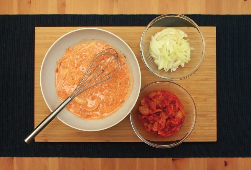 Schälchen mit Zwiebelstreifen und geschnittenem Kimchi neben einer Schüssel Teig mit Schneebesen