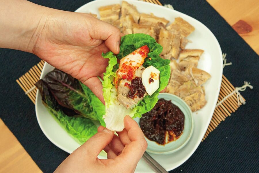 Hände wickeln Fleisch, Kimchi und Knoblauch in ein Salatblatt