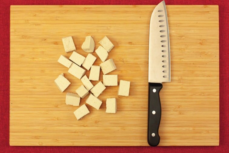 Tofuwürfel und ein Messer auf einem Holzbrett