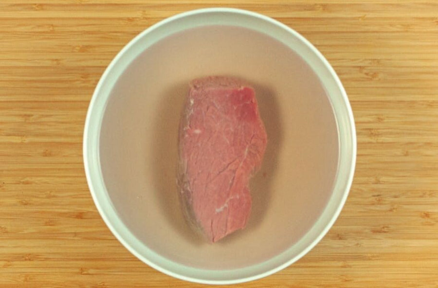 Ein Stück Rindfleisch in einer Schüssel mit kaltem Wasser