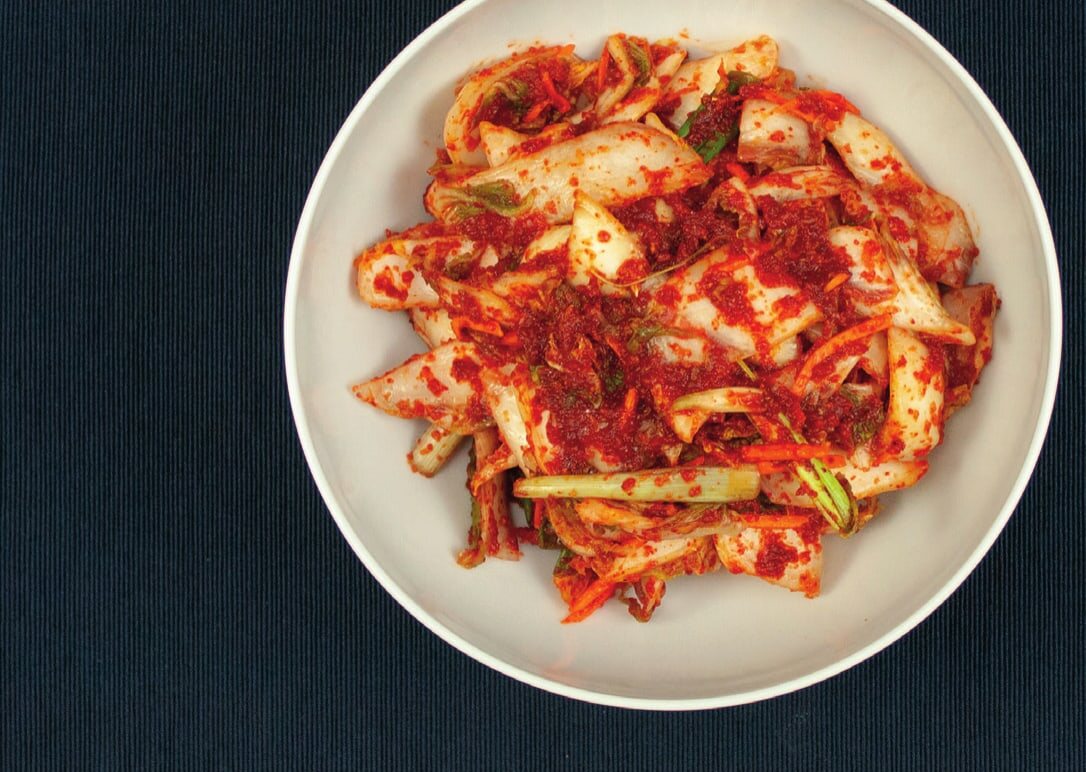 Frischer Kimchi mit Sesam auf einer ovalen Platte, daneben ein Bügelglas mit eingefülltem Kimchi