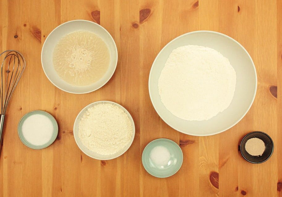 Schalen mit Hefewasser, Mehl, Zucker, Salz und Trockenhefe, daneben ein Schneebesen