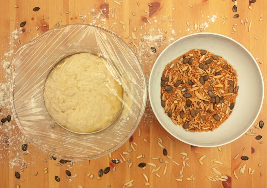 Gegangener Hefeteig in einer abgedeckten Schüssel, daneben eine Schale mit Füllung aus Zucker, Zimt, Mandeln und Kürbiskernen