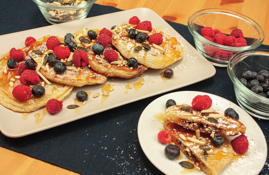 Hotteok mit Beeren, Mandelstiften, Kürbiskernen und Honig auf einer Platte und einem kleinen Teller