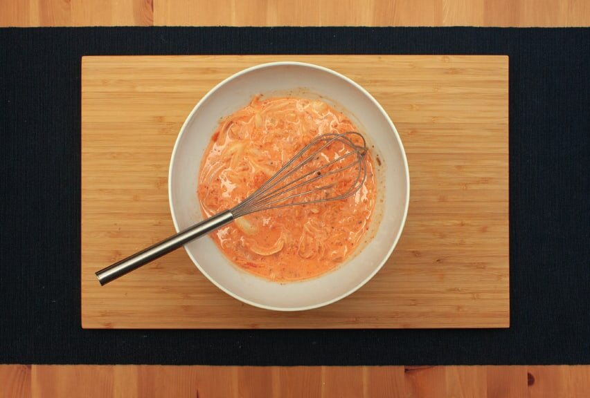 Schüssel mit Teig, Kimchi und Zwiebeln, darin ein Schneebesen