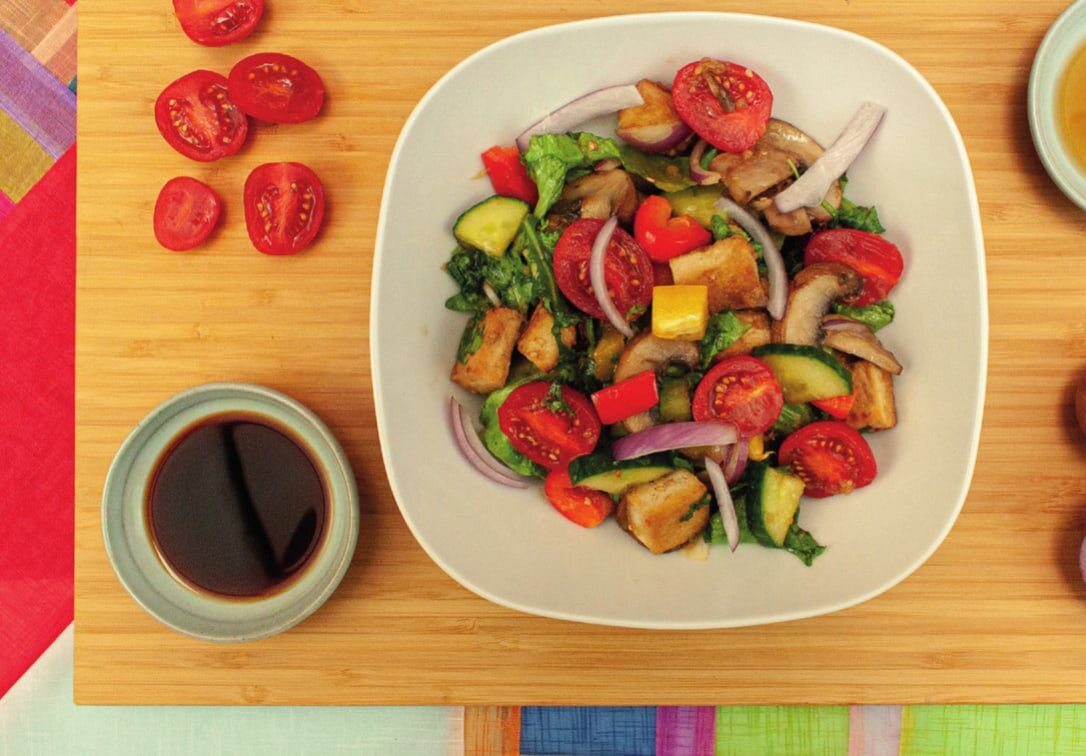 Salat mit Cherrytomaten, gebratenem Tofu, Champignons, Gurke, Paprika und roter Zwiebel, daneben Schälchen mit Sojasoße und Öl